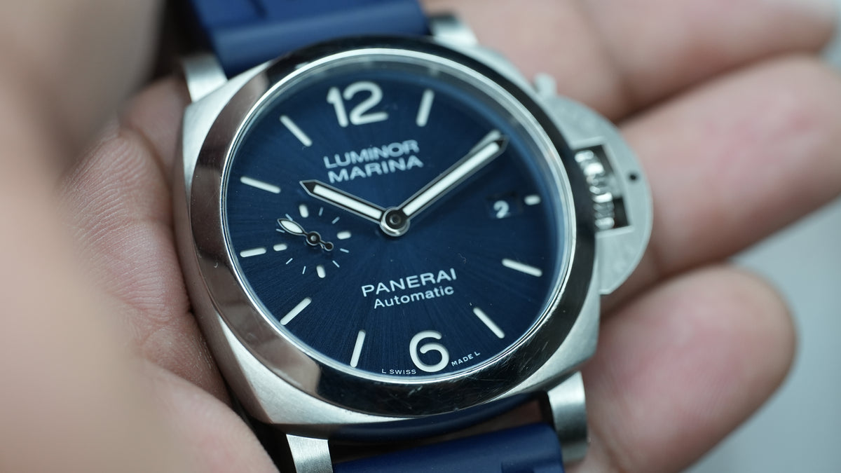 Panerai Luminor Marina PAM01370 held in hand, showing blue dial and surface scratches along the lower polished bezel.